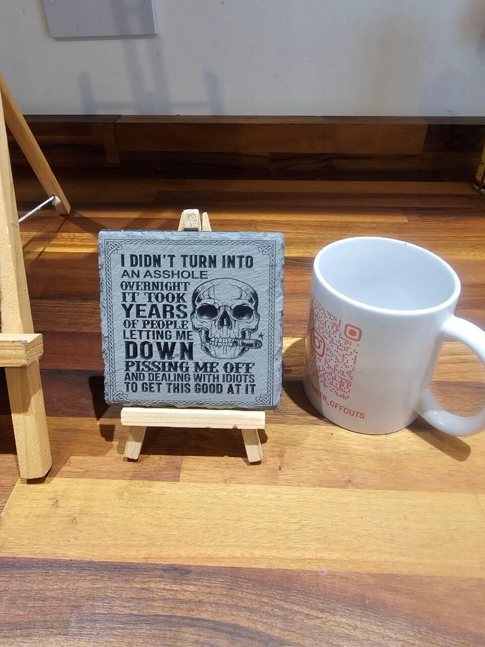 Engraved Slate Coaster. I Didn’t Turn Into An Asshole Overnight displayed on easel with mug.