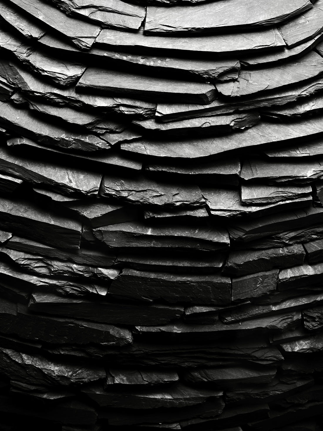 Curved wall made of stacked dark grey slate tiles.