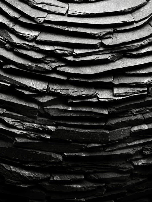 Curved wall made of stacked dark grey slate tiles.