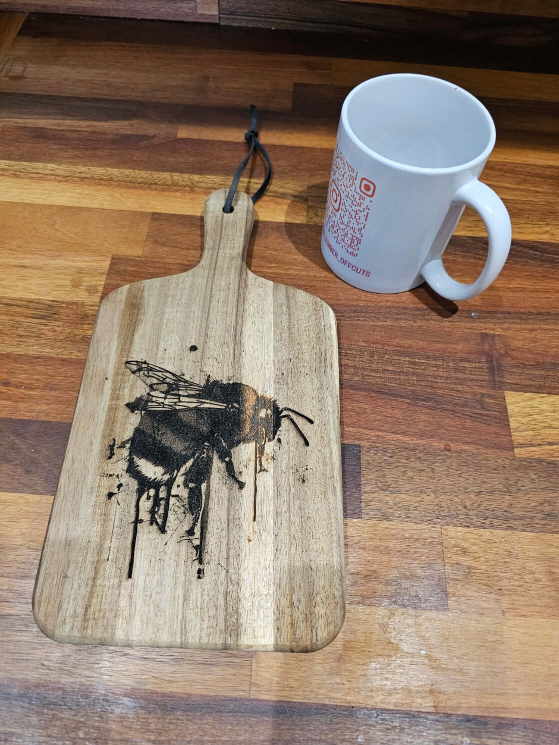 Handcrafted Engraved Bee Serving Board with bee design next to a white mug on a wooden surface.