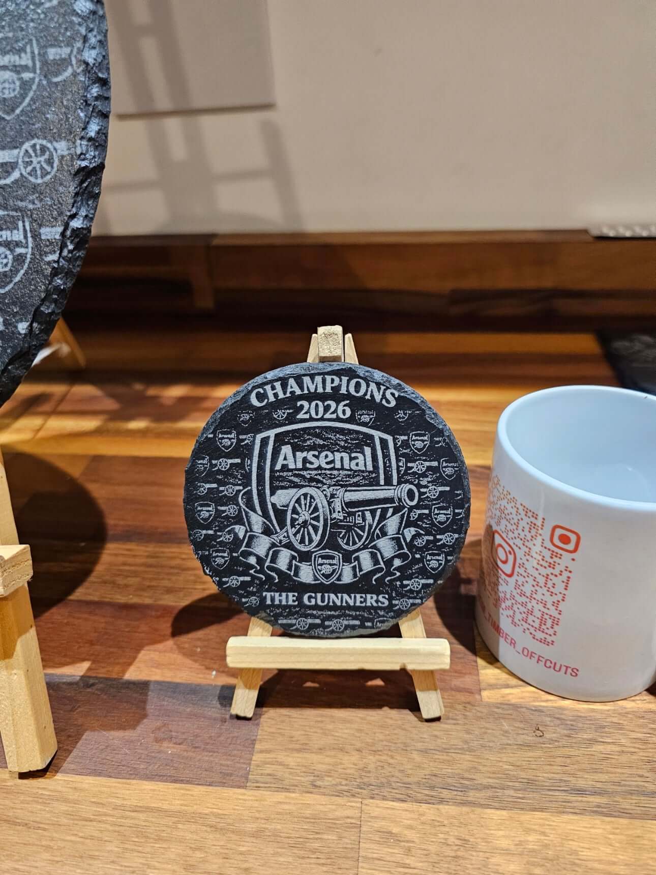 Arsenal Champions 2026 Engraved 300mm round slate plaque on display with mug, showcasing the club's memorabilia.