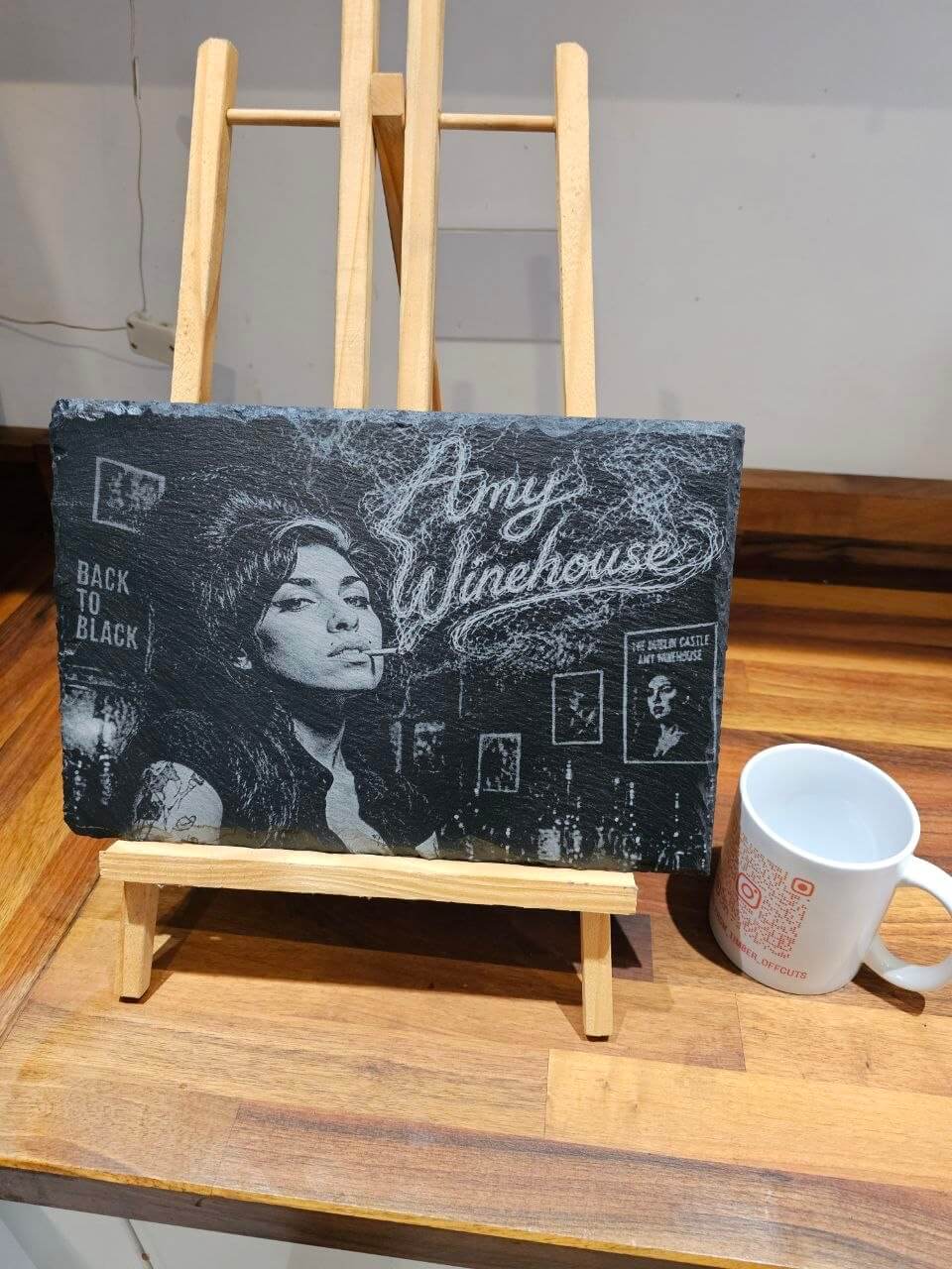 Amy Winehouse Back to Black Engraved Slate Plaque HandmadeUK displayed on an easel with a mug beside it.