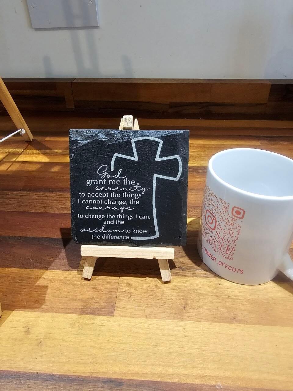 Engraved Slate Coaster. Serenity Prayer Cross 10cm x 10cm displayed on a mini easel next to a mug.